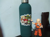 A green water flask with a Chrono Trigger sticker on it and a Krillin figurine touching it.