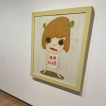 A photo of a Yoshitomo Nara piece of a young girl with a shirt that says NO WAR'